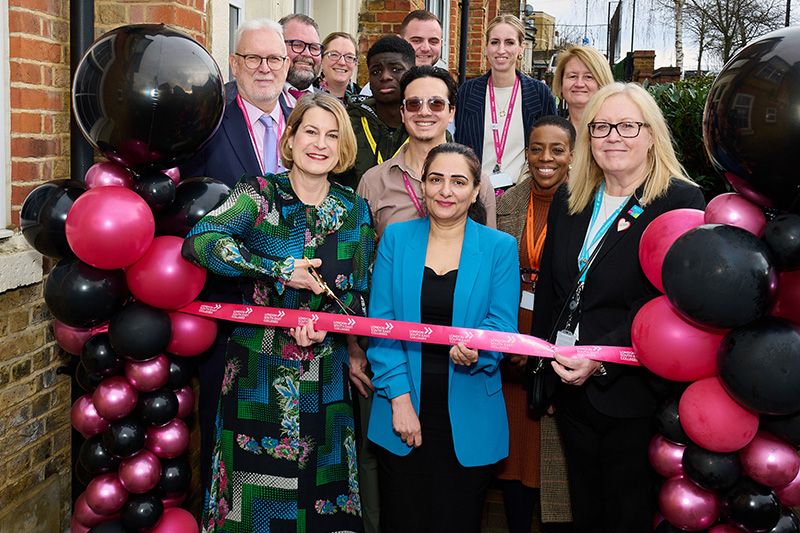 a crowd surrounds a lady cutting a ribbon at the door